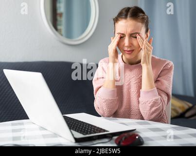 Junge Frau, die nach der Arbeit am Laptop Augenschmerzen hatte Stockfoto