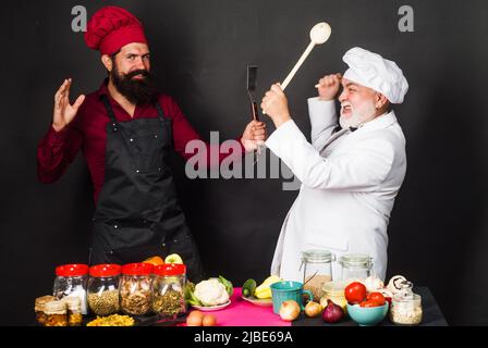 Kulinarischer Kampf. Zwei Köche in Uniform kämpfen in der Küche. Wettbewerb des Küchenchefs. Leckeres Essen. Stockfoto