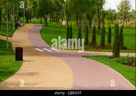Gepflasterte Steinwege mit farbigen roten und gelben Ziegeln mit Fahrradmarkierungen im Grünen, städtische Landschaftsgestaltung mit Pflanzen im Landschaftsdesign, Park auf Stockfoto