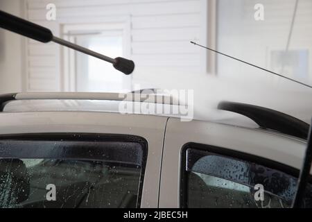 Ein Prozess der Spülung von SOAP sud auf dem silbernen Autodach mit Druckwasserstrom an der SB-Autowaschstation Stockfoto