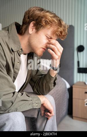 Unglücklicher, tausendjähriger Ingwer-Freiberufler, der Nasenrücken massiert Stockfoto