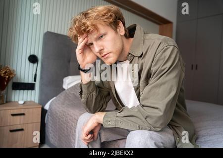 Junger Ingwer mit schmerzhaftem Kopf auf dem Bett sitzend selektiver Fokus Stockfoto