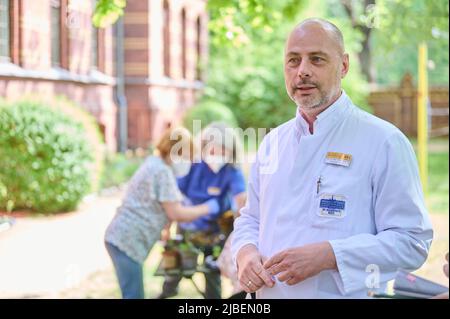 Berlin, Deutschland. 10.. Mai 2022. Torsten Kratz, Facharzt für Neurologie, Psychiatrie und gerontologische Psychiatrie, spricht im „Grünen Behandlungsraum“ des Evangelischen Krankenhauses Königin Elisabeth Herzberge darüber, wie Gartentherapie helfen kann. Im Hintergrund arbeitet der Gartentherapeut mit einem Patienten zusammen. (To dpa 'Graben, Jäten, Pflanzen: Gartentherapie ohne Medikamente') Quelle: Annette Riedl/dpa/Alamy Live News Stockfoto