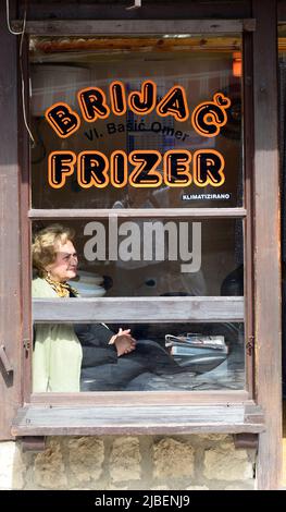 Eine bosnische Frau, die aus dem Fenster eines lokalen Friseursalons in Baščaršija, Sarajevo, Bosnien und Herzegowina blickt. Stockfoto