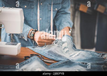 Schneiderarbeit mit Jeans aus blauem Denim. jeanshose reparieren. Stockfoto