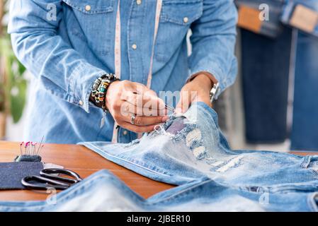 Schneiderarbeit mit Jeans aus blauem Denim. jeanshose reparieren. Stockfoto