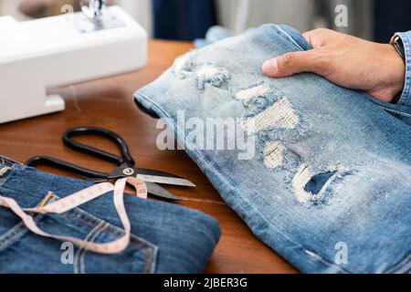 Schneiderarbeit mit Jeans aus blauem Denim. jeanshose reparieren. Stockfoto