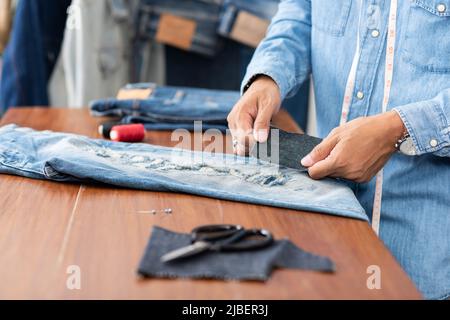 Schneiderarbeit mit Jeans aus blauem Denim. jeanshose reparieren. Stockfoto