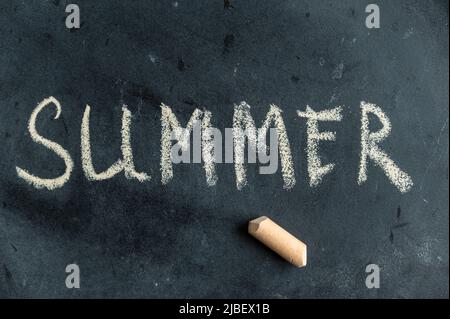 SOMMER. Der Name der Saison ist in gelber Kreide auf einer schwarzen Tafel geschrieben. Handgeschriebener Text. Daneben liegt ein Stück farbige Kreide. Stockfoto