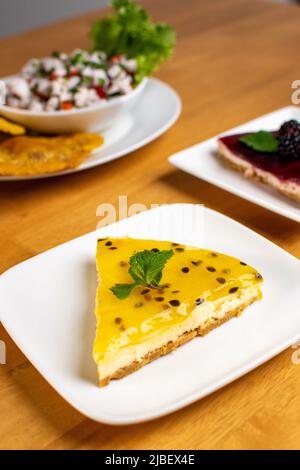 Schöner Passionsfrucht-Käsekuchen mit Ceviche in einem Holztisch und weißem Teller Stockfoto