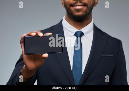 Nahaufnahme eines schwarzen Geschäftsmannes, der ein leeres Smartphone-Modell hält und der Kamera den Kopierraum zeigt Stockfoto