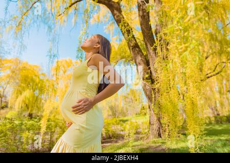 Schwanger gesunde Frau atmen saubere Luft während der Schwangerschaft in frischen Frühlingswald Natur. Asiatische Mädchen halten erwartet Bauch in Glück und Stockfoto