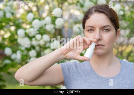 Kaukasische Frau verwendet ein Nasenspray, während sie im Park spazieren geht. Stockfoto