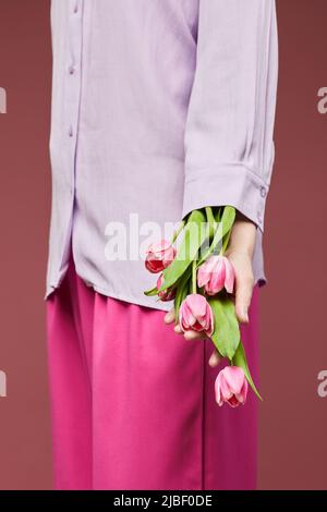 Minimale Nahaufnahme einer jungen Frau, die ein rosa Outfit trägt und zarte rosa Tulpen trägt Stockfoto