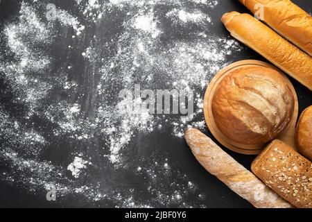 Auswahl an frischem Brot auf schwarzem Hintergrund mit Mehl, Draufsicht, Kopierraum. Hausgemachte frisch gebackene verschiedene Weizen- und Roggenbrote. Stockfoto