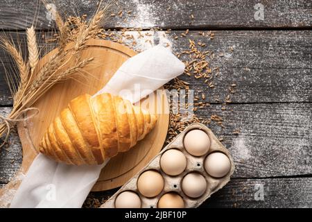 Frisch gebackenes Croissant in einer Bäckerei auf Holzhintergrund mit Eiern, Konditornahrung, Brot- und Rollenproduktionskonzept, Draufsicht, Flachlage Stockfoto