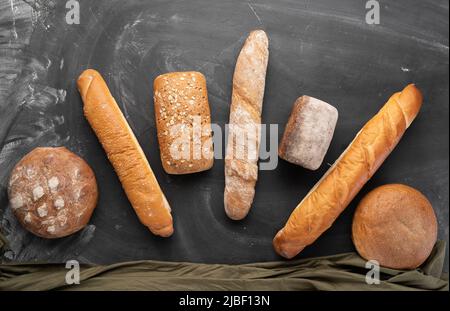 Frisches Brot auf schwarzem Hintergrund, Draufsicht. Hausgemachte, frische Backwaren verschiedener Weizen- und Roggenbrote aus der Nähe. Stockfoto