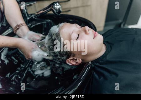 Frau, die Shampoo anwendet und die Haare des Kunden massiert. Eine Frau, die sich beim Friseur die Haare wäscht. Hochwertige Fotos Stockfoto