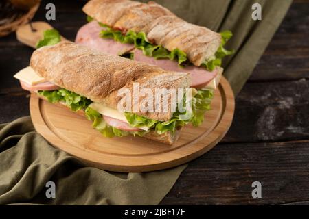 Zwei frische Sandwiches mit Schinken, Käse, Salat auf einem Holzbrett. Stockfoto