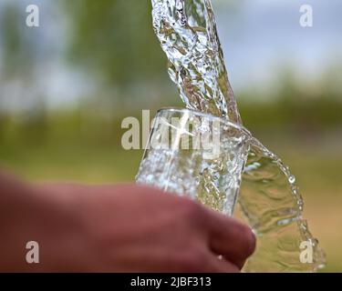 Wasser wird in ein Glas gegossen und fließt über. Stockfoto