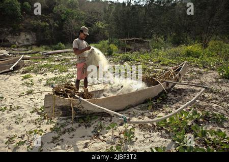 Ein Subsistenzfischer, der sein Fischernetz am Strand von Tarimbang in Tabung, East Sumba, East Nusa Tenggara, Indonesien, abrollt. Stockfoto