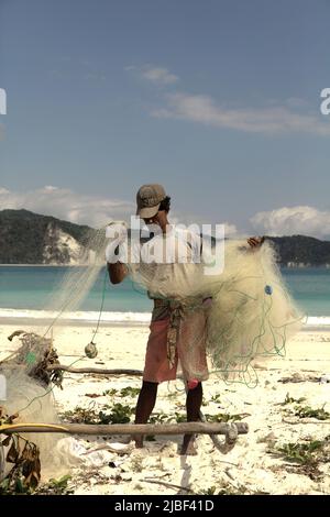 Ein Subsistenzfischer, der sein Fischernetz am Strand von Tarimbang in Tabung, East Sumba, East Nusa Tenggara, Indonesien, abrollt. Stockfoto