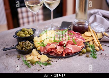 Zwei Gläser Weißwein und italienische Antipasto-Fleischplatte in der heimischen Küche Stockfoto