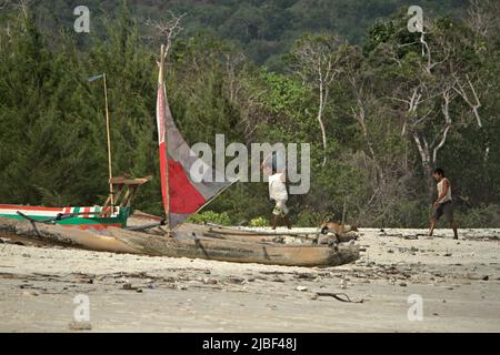 Ein Fischer trägt einen kanister auf der Schulter, während er auf Holzkanus am Tarimbang Beach in Tabundung, East Sumba, East Nusa Tenggara, Indonesien, zuläuft. Stockfoto