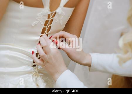 Brautjungfern helfen der Braut, ihr Hochzeitskleid anzuziehen Stockfoto