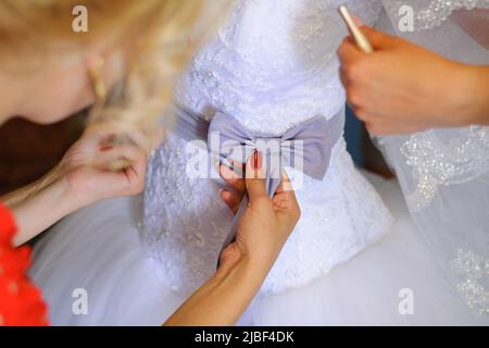 Brautjungfern helfen der Braut, ihr Hochzeitskleid anzuziehen Stockfoto