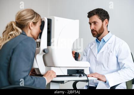 Der männliche Augenarzt überprüft die Sehkraft eines Patienten in einem Augenarztgeschäft oder in einer Augenklinik Stockfoto