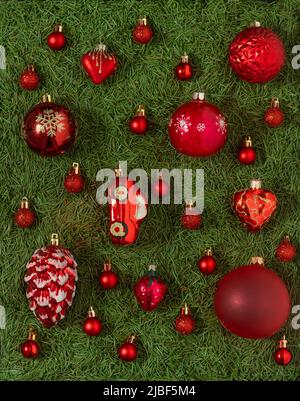 Eine Reihe von verschiedenen roten Weihnachtsspielzeug auf einem grünen Hintergrund von Weihnachtsbaum Nadeln. Rote Kugel. Einrichtung und Dekoration. Neujahrskonzept. Stockfoto