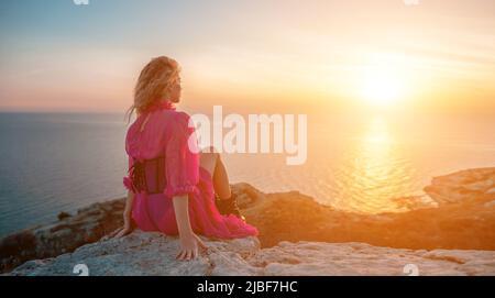 Schöne junge kaukasische Frau mit lockigen blonden Haaren und Sommersprossen. Niedliches Rotschopf-Frauenportrait in einem rosa langen Kleid, das auf einem vulkanischen Felshochsprung posiert Stockfoto