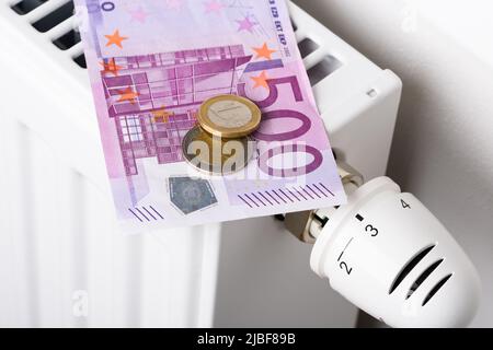 500-Euro-Banknote mit Münzen auf Heizkörper-Batterie mit Thermostat-Temperaturregler. Konzept teurer Heizkosten und steigender Energie b Stockfoto