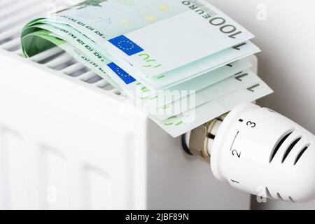 100 Euro Banknoten in Heizkörper-Batterie mit Thermostat-Temperaturregler. Konzept teurer Heizkosten und steigender Energiebillimpreise Stockfoto