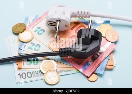 Zwei europäische Stromstecker auf Euro-Banknoten und Münzen auf blauem Hintergrund. Konzept von teuren Stromkosten und steigenden Stromrechnungen Stockfoto