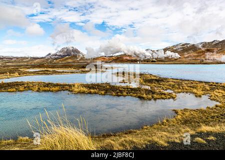 Hinter einem blauen See in der Mitte Islands liegt das Geothermalgebiet Myvatn Stockfoto