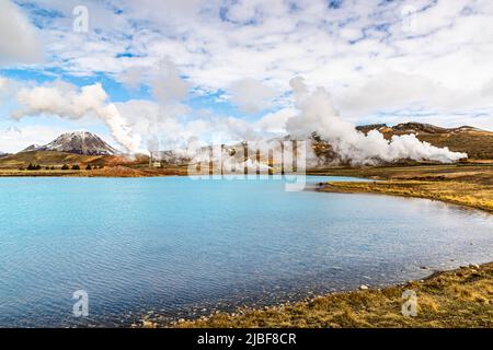 Hinter einem blauen See in der Mitte Islands liegt das Geothermalgebiet Myvatn Stockfoto