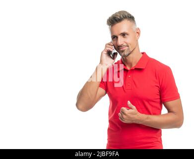 Fröhlicher Mann in rotem T-Shirt spricht auf Smartphone isoliert auf weißem Hintergrund. Daumen hoch Stockfoto