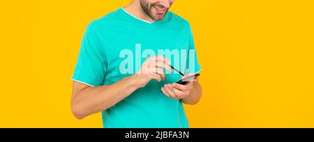 Abgeschnitten unrasiert junger Mann hod Telefon und Stift auf gelbem Hintergrund, Technologie Stockfoto