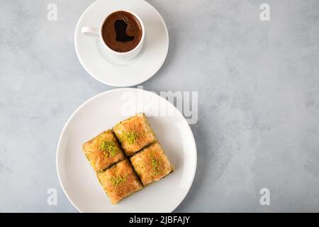 Pistazien-Baklava auf einem weißen Teller mit türkischem Kaffee.Ein Teller mit traditionellem Baklava auf weißem Hintergrund Stockfoto
