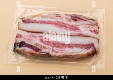 Italienische Guanciale, Scheiben trocken gehärtete Schweinebacke in Vakuum verpackt versiegelt für Sous-Vide-Kochen isoliert auf hellbraunem Hintergrund Stockfoto