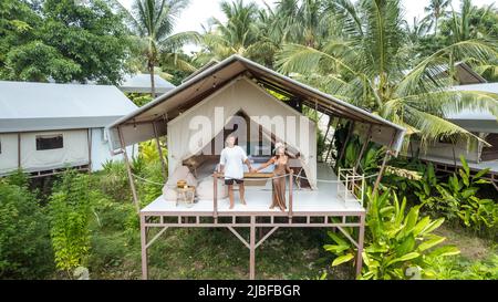 Junges Touristenpaar, das vor einem luxuriösen Campingzelt in einem tropischen Dschungel steht Stockfoto