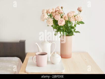 Guten, gemütlichen Morgen. Blumenstrauß in Vase auf dem Tisch. Hotelzimmer mit Bett. Check-in im Hotel. Ruhe und Entspannung. Kaffee im Bett. Romantisches Frühstück Stockfoto