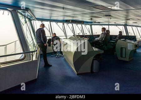 Auf der Brücke der Smyril-Line-Fähre Norröna blicken drei Besatzungsmitglieder durch dichten Nebel auf das Meer hinaus. Kontrollkonsolen mit zahlreichen Anzeigelampen und Monitoren säumen den Raum. Stockfoto