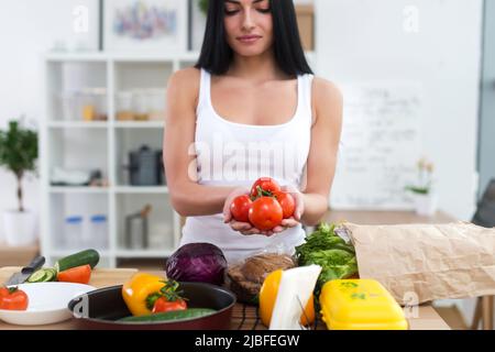 Mädchen, das in der Küche steht und rote Tomaten in den Händen hält. Hausfrau nimmt frische Zutaten für Gemüsesalat Stockfoto