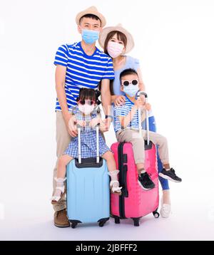Glückliche Familie in Gesichtsmasken mit Koffern, die isoliert auf weißem Hintergrund stehen. Menschen bereit für den Sommerurlaub, sicheres Reisekonzept Stockfoto