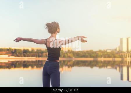 Frau, die den Sonnenuntergang genießt, die Arme ausgestreckt und das Gesicht am Himmel angehoben. Stockfoto