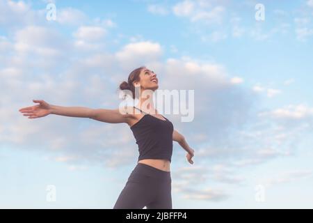 Frau, die den Sonnenuntergang genießt, die Arme ausgestreckt und das Gesicht am Himmel angehoben. Stockfoto