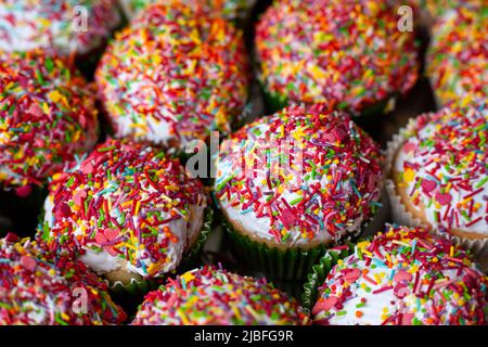 Hausgemachte Cupcakes dekoriert Zucker bestreut in Makro. Gruppe von hausgemachten Vanille-Muffins weiß glasiert bunten Dekoration. Sweet Cake Hintergrund. Stockfoto